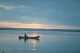 A man in a canoe, paddling into the sunset. "